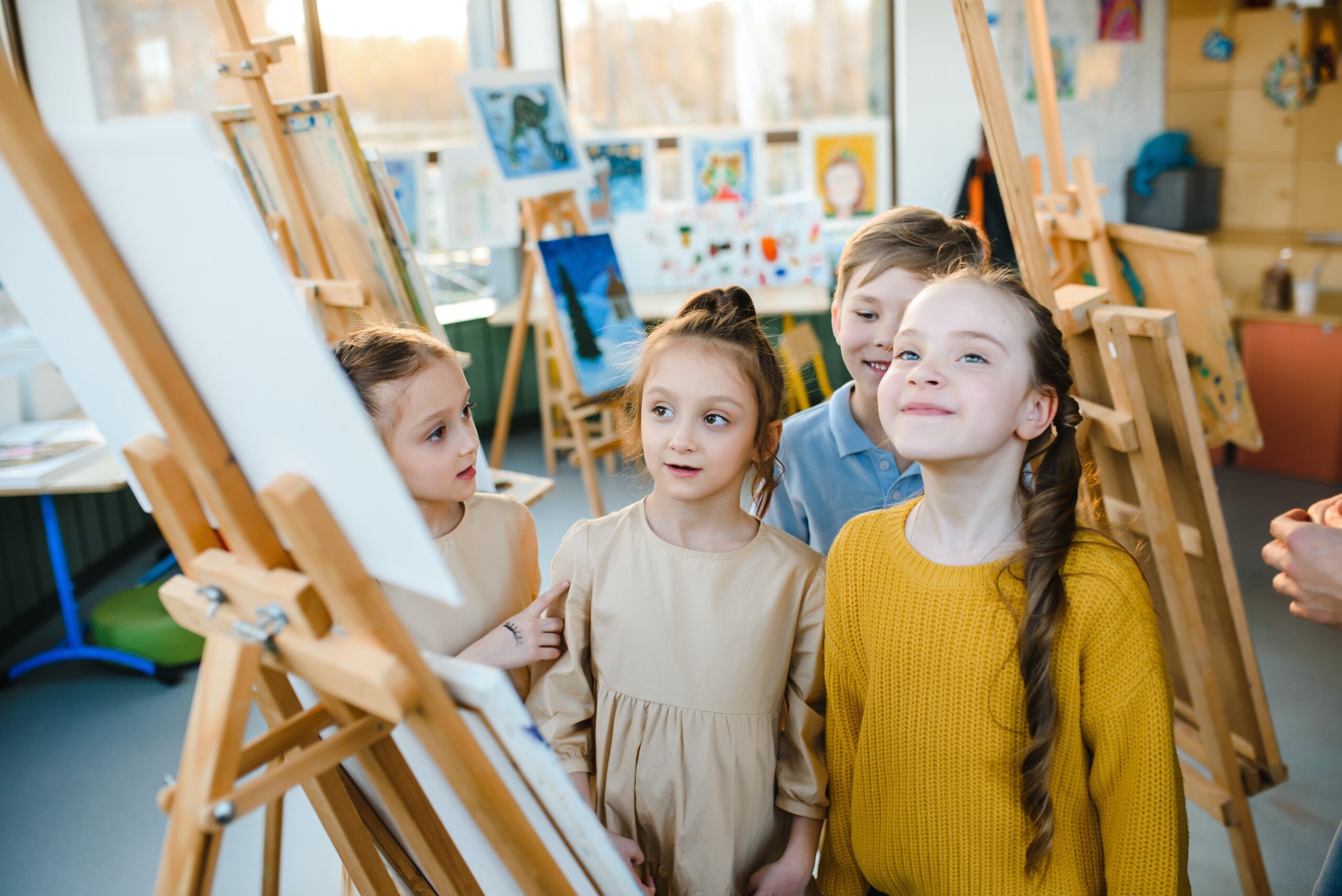 Four young children standing next to an easel in a classroom