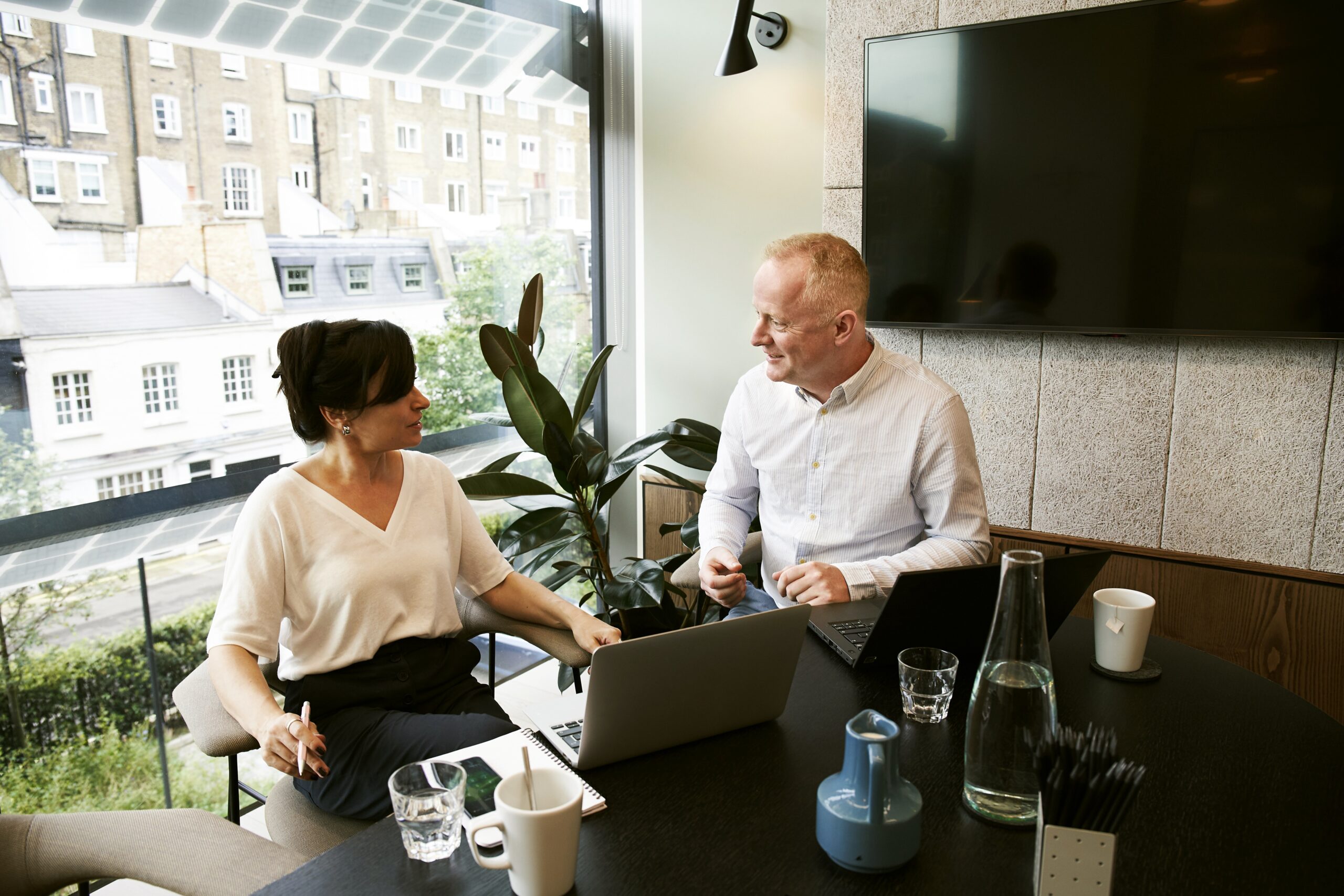 Man and woman talking in an office at a desk over a laptop