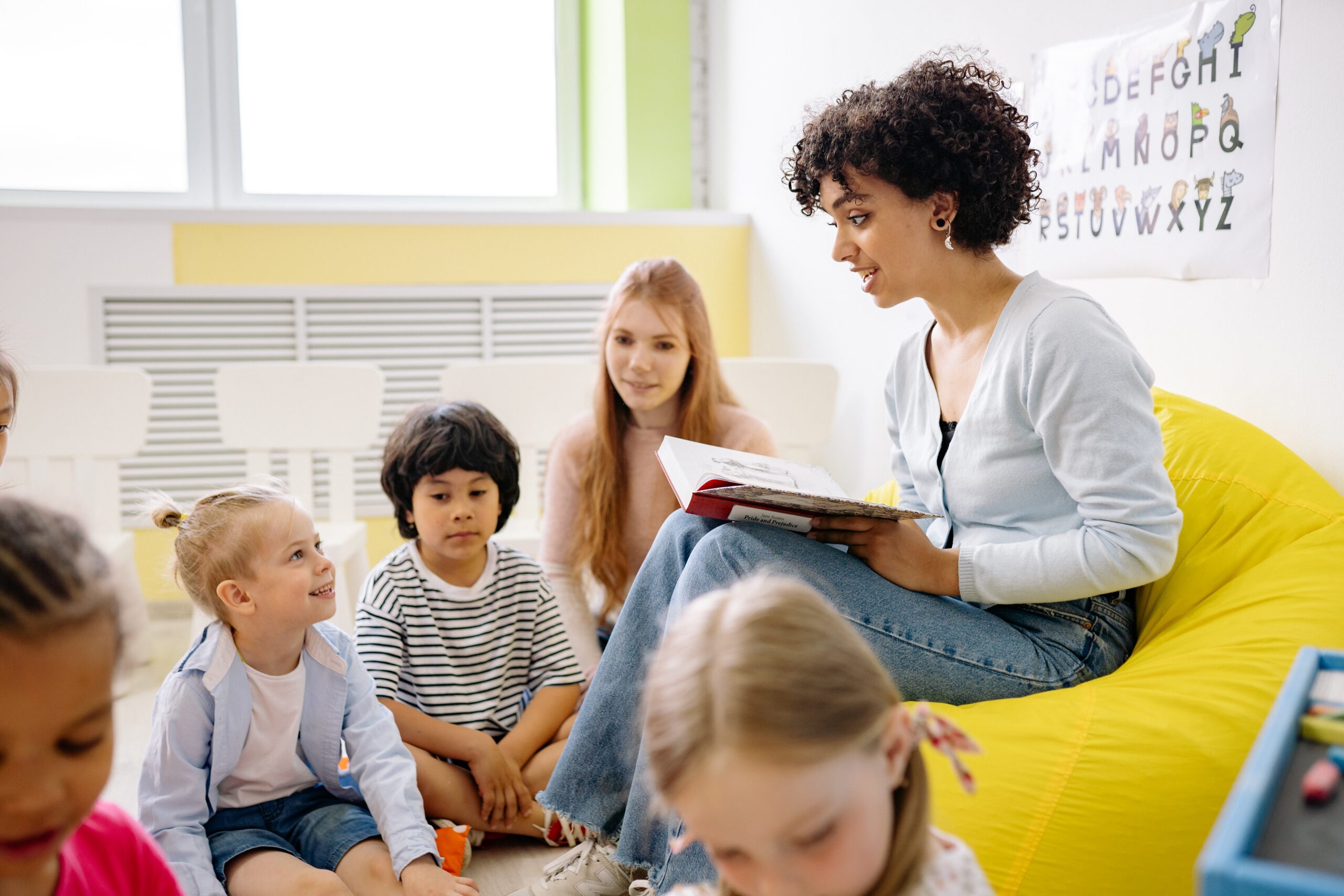 Female teacher sitting with and reading to young children in a classroom