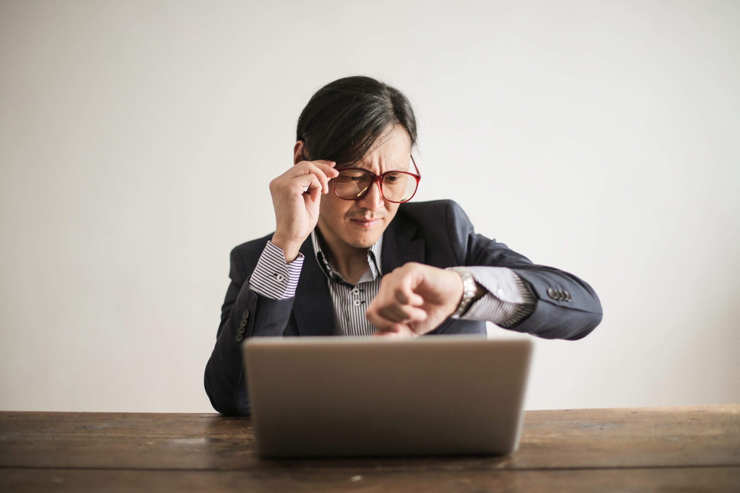 Man in suit sitting at laptop looking concernedly at his watch